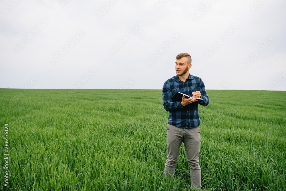 Young agronomist holds notebook in green wheat field. Agribusiness concept. agricultural engineer standing in a wheat field with a tablet in summer Young agronomist holds notebook in green wheat field. Agribusiness concept. agricultural engineer standing in a wheat field with a tablet in summer