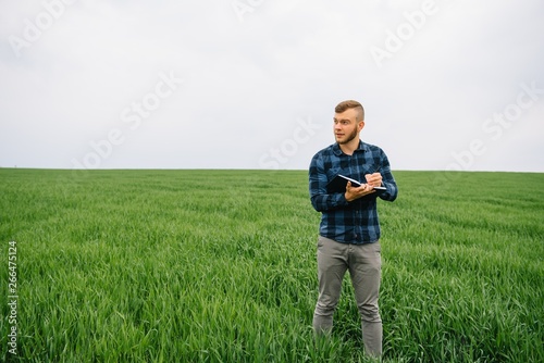 Young agronomist holds notebook in green wheat field. Agribusiness concept. agricultural engineer standing in a wheat field with a tablet in summer © Serhii