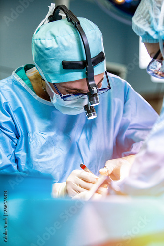 Surgeon and his assistant performing cosmetic surgery on nose in hospital operating room. Nose reshaping, augmentation. Rhinoplasty.