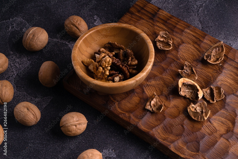 Walnut kernels in wooden bowl and whole walnuts on blue slate table. Healthy nuts and seeds composition.