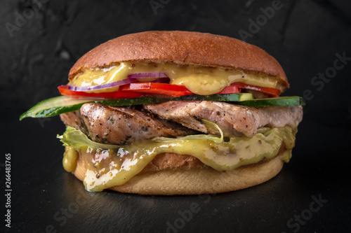 Juicy fresh delicious hamburger. Juicy burger with chicken grilled fillets, cheese chedar, tomatoes, cucumbers, lettuce and onions on a fresh bun on the background of coals. The burger menu.