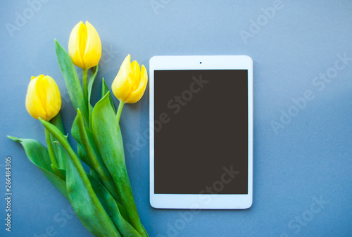 Fototapeta Naklejka Na Ścianę i Meble -  Bouquet of beautiful yellow tulips and tablet on violet background with copyspace. Spring concept.
