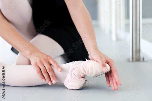 Female ballet teacher is stretching and making string exercises with little ballerina kid in classical dance school. Close up of foot in ballet point shoose, legs and hand.