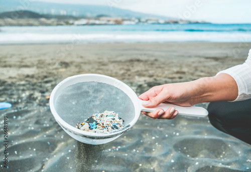 Young woman cleaning microplastics from sand on the beach - Environmental problem, pollution and ecolosystem warning concept - Focus on hand photo