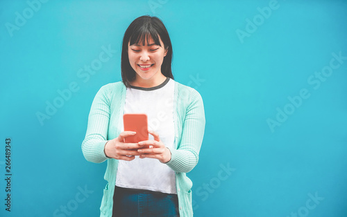 Asian woman using smartphone with blue background - Happy chinese girl having fun with new trends technology - Fashion, tech and millennial generation activity - Focus on face photo