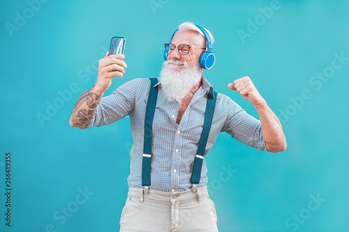 Senior hipster man using smartphone app for creating playlist music - Trendy tattoo guy having fun with mobile phone technology - Tech and joyful elderly lifestyle concept - Focus on his face