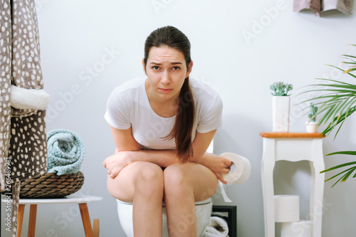 Young woman suffering from constipation on toilet bowl at home photo