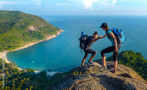 Obraz na plátne Man and woman hiking on the top of cliff in summer mountains at morning time and