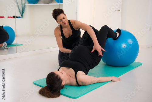 Pregnant woman does pilates exercises with the help of her teacher. Exercise with pilates ball.