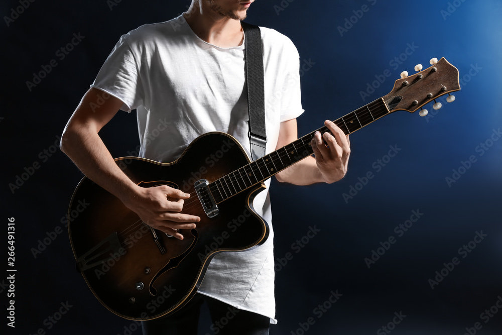 Obraz premium Handsome young man playing guitar on dark background