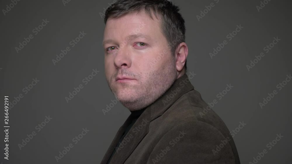 Portrait of brunette middle-aged businessman in suit turns to camera watching calmly into camera on gray background. Portrait of brunette middle-aged businessman in suit turns to camera watching calmly into camera on gray background.