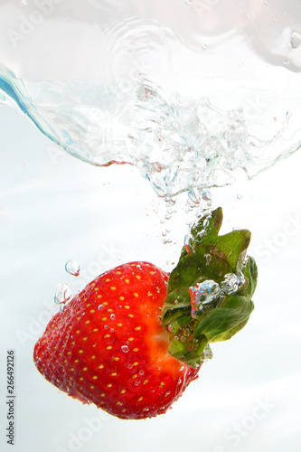 Fresh strawberri splashing into water on white