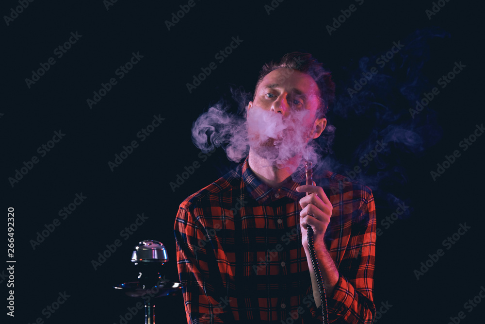 Young man smoking hookah on dark background