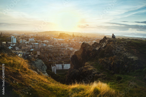 Top view from the mountains of Edinburgh and a seated tourist looking out over the city at sunset. From Arthur's Seat. Edinburgh, Scotland, United Kingdom