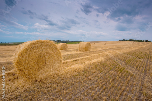 Hay bales under a cloudy sunset sky on a harvested wheat field.