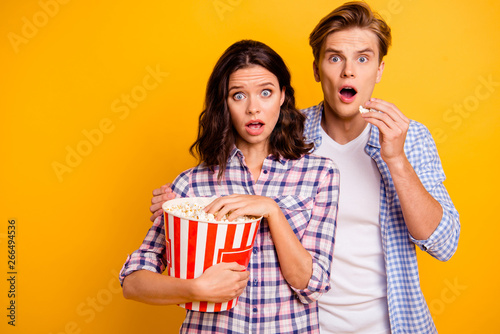 Close up photo of pair  he him his she her lady boy eyes wide opened pop corn in mouth close to each other afraid of horror film wearing casual plaid shirts outfit isolated on yellow background