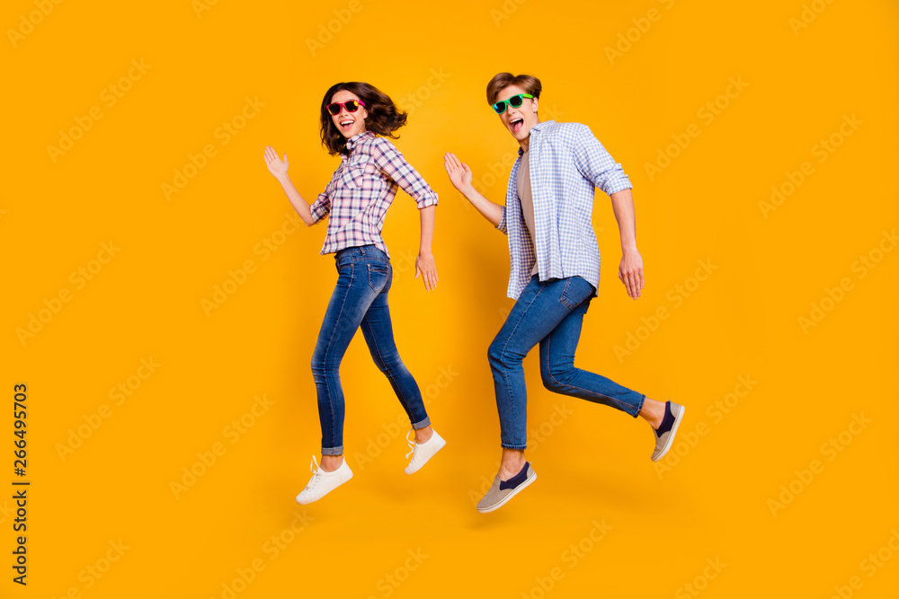 Close up full length body size photo of pair in summer specs he him his she her lady boy make dance moves jumping high fooling around wearing casual plaid shirt outfit isolated on yellow background Close up full length body size photo of pair in summer specs he him his she her lady boy make dance moves jumping high fooling around wearing casual plaid shirt outfit isolated on yellow background
