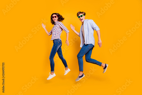 Close up full length body size photo of pair in summer specs he him his she her lady boy make dance moves jumping high fooling around wearing casual plaid shirt outfit isolated on yellow background