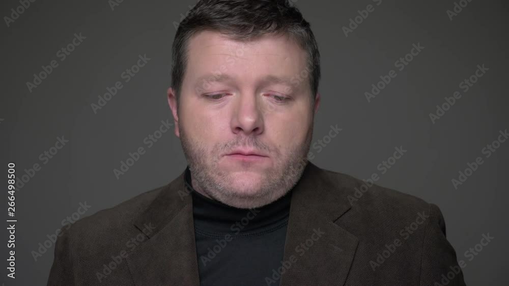 Portrait of sad brunette middle-aged businessman in suit watching miserably into camera on gray background. Portrait of sad brunette middle-aged businessman in suit watching miserably into camera on gray background.