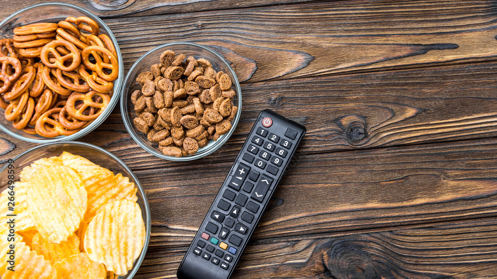 chips, crackers, snacks, TV remote control on the background of a wooden table. free time. leisure.