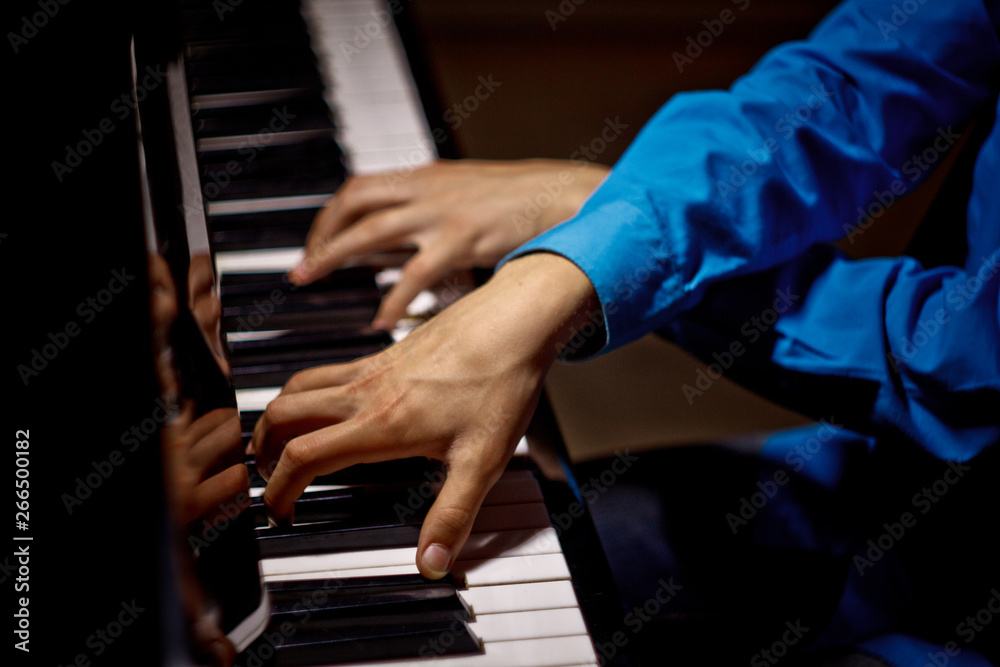 Obraz premium two male hands on the piano. palms lie on the keys crosswise and play the keyboard instrument in the music school. student learns to play. hands pianist. black dark background. top view