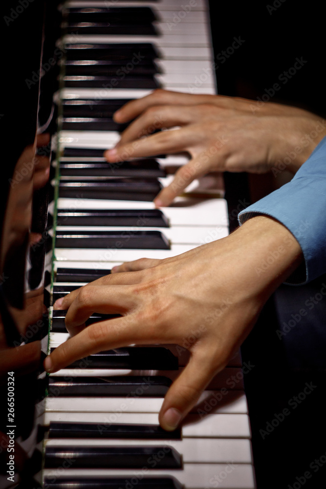 Obraz premium two male hands on the piano. palms lie on the keys crosswise and play the keyboard instrument in the music school. student learns to play. hands pianist. black dark background. top view. vertical