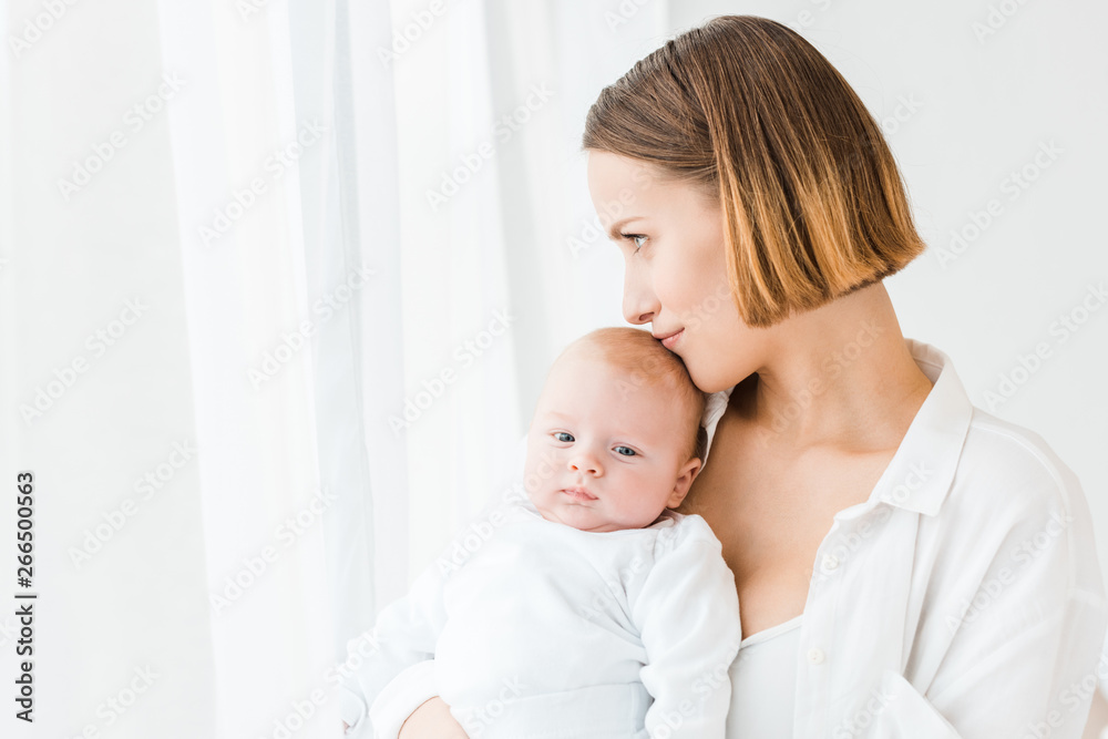Smiling young mother in white shirt holding baby at home Smiling young mother in white shirt holding baby at home