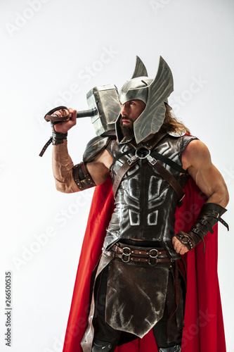 Long hair and muscular male model in leather viking's costume with the big hammer cosplaying Thor isolated on white studio background. Half-lenght portrait. Fantasy warrior, antique battle concept.