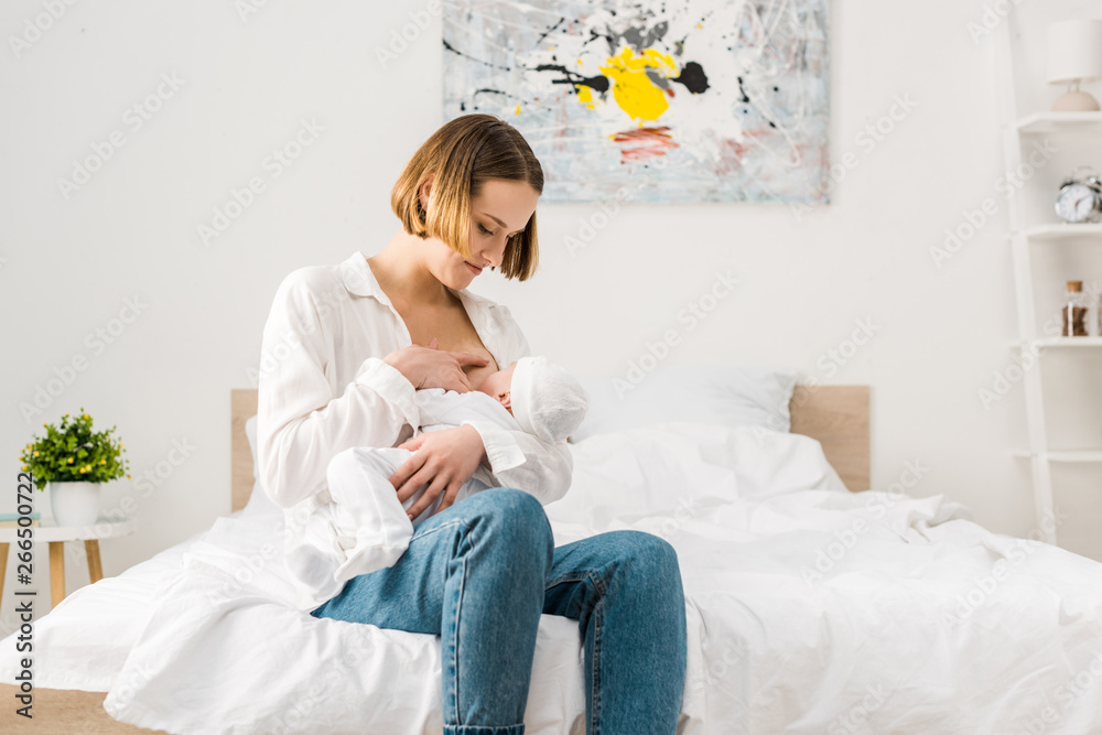 Mother in jeans sitting on bed and breastfeeding baby Mother in jeans sitting on bed and breastfeeding baby