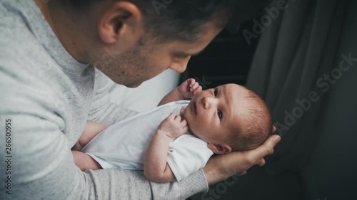 Newborn baby in the arms of his adoring father looks up to face of daddy. Wide eyed infant cradled in arms of man looking down at the child. Slow motion.