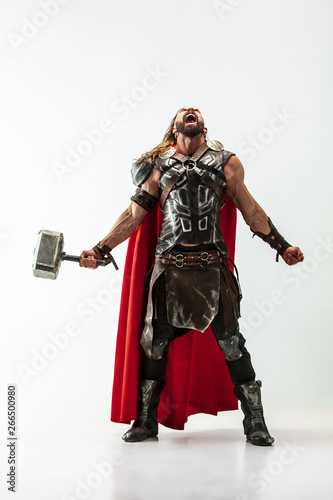 Long hair and muscular male model in leather viking's costume with the big hammer cosplaying Thor isolated on white studio background. Full-lenght portrait. Fantasy warrior, antique battle concept. photo