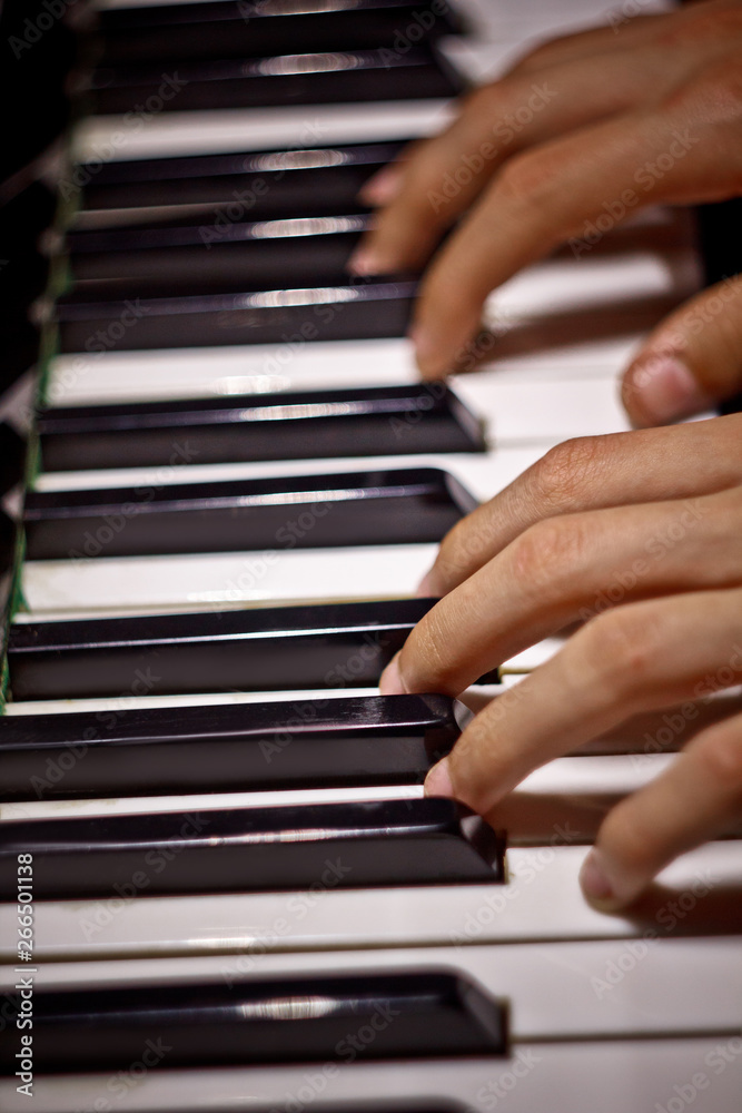 Obraz premium two male hands on the piano. palms lie on the keys and play the keyboard instrument in the music school. student learns to play. hands pianist. black dark background. top view. vertical