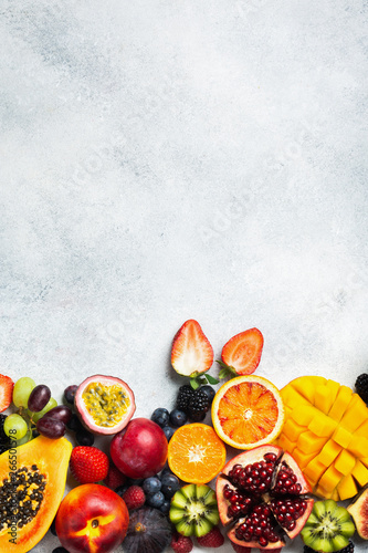 Fototapeta Naklejka Na Ścianę i Meble -  Healthy raw rainbow fruits background, mango papaya strawberries oranges passion fruits berries on oval serving plate on light kitchen top, top view, copy space, selective focus