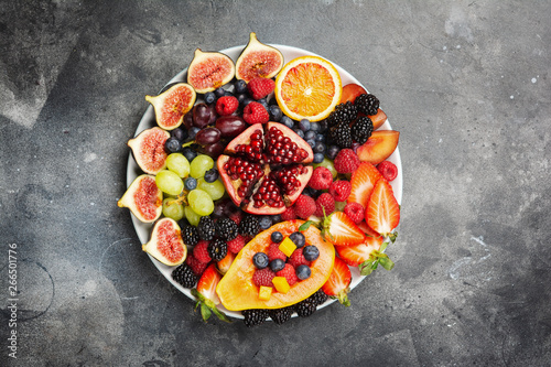 Fototapeta Naklejka Na Ścianę i Meble -  Delicious fruit platter mango papaya oranges passion fruits berries on round serving plate on dark concrete background, overhead view, selective focus, copy space