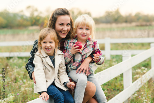 Pretty young mother having fun together with her daughters. Happy loving family. Stylish lovely mother with kids. Family enjoing and playing on meadow at autumn sunset background. Fashion family look.