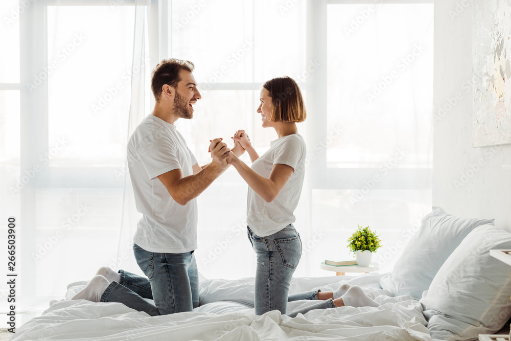 Happy couple holding hands and looking at each other in bedroom Happy couple holding hands and looking at each other in bedroom