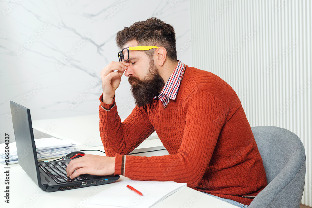 Tired man with laptop computer at working place. Bearded man overworked at office. Stressed handsome business man. Feeling exhausted. Young man having stressful time working on laptop