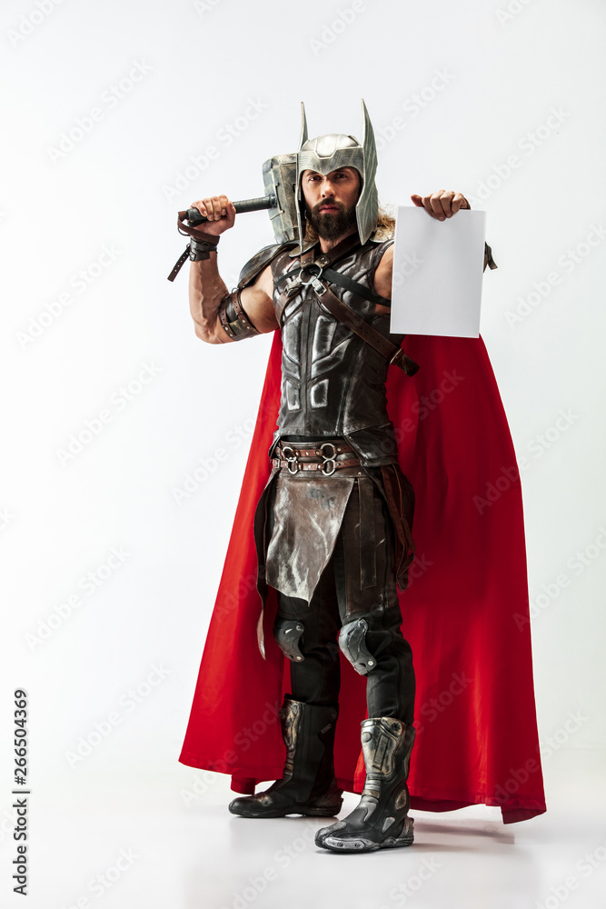 God of thunder. Blonde long hair and muscular male model in leather viking's costume with the big hammer cosplaying Thor on white studio background. Fantasy warrior, business concept. Copy space.