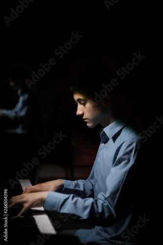 young man sitting at the piano. boy emotionally plays the keyboard instrument in the music school. student learns to play. hands pianist. black dark background. vertical