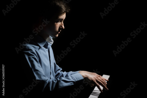 young man sitting at the piano. boy emotionally plays the keyboard instrument in the music school. student learns to play. hands pianist. black dark background