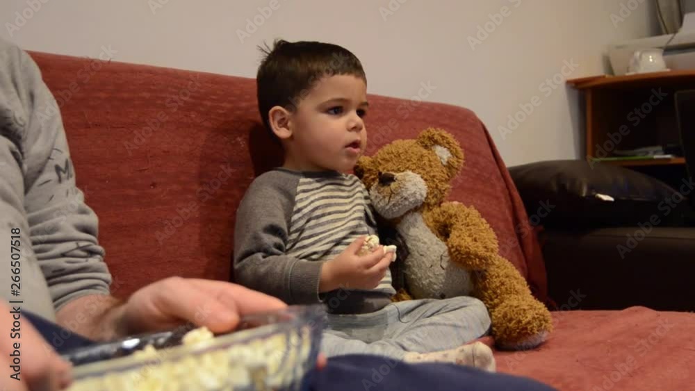 Father and two years old son watching tv together with pop corns. Father and two years old son watching tv together with pop corns.