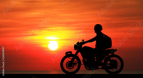 Silhouette biker with his motorbike on blurry blue sky background