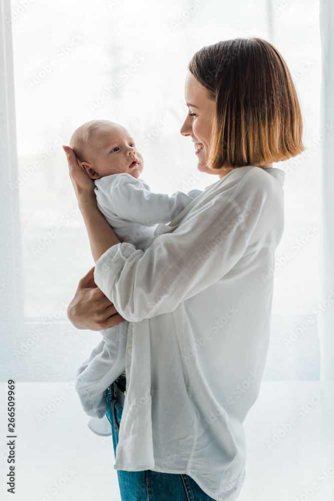 Smiling mother in white shirt holding baby at home