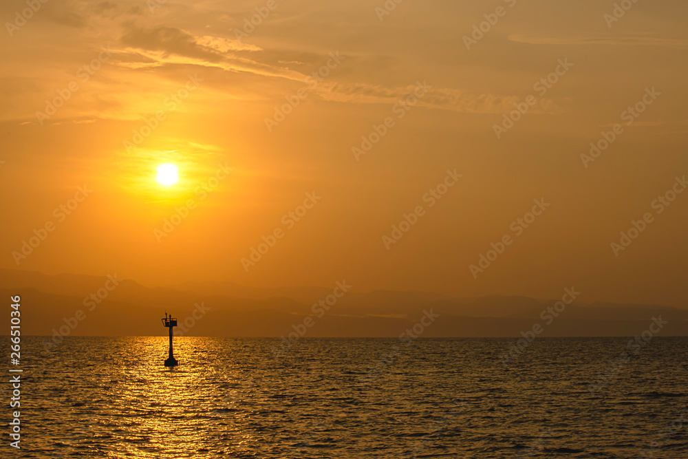 Golden light of sunrise behind the mountains and the shadow of signal lamp for sailing in the sea.