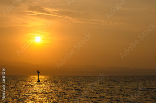 Golden light of sunrise behind the mountains and the shadow of signal lamp for sailing in the sea. © Nueng