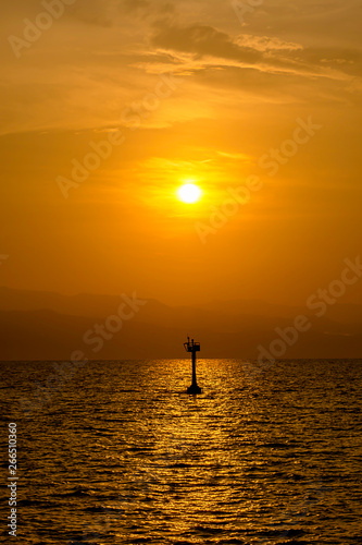 Golden light of sunrise behind the mountains and the shadow of signal lamp for sailing in the sea.