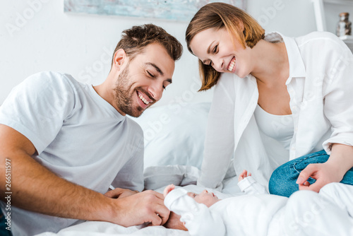 Happy young parents looking at baby on bed