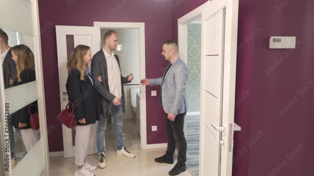 Young Caucasian Married Couple Standing in Lobby of New Apartment Property and They Recieve Keys from Realtor Real Estate Broker. Light Camera Movement Young Caucasian Married Couple Standing in Lobby of New Apartment Property and They Recieve Keys from Realtor Real Estate Broker. Light Camera Movement