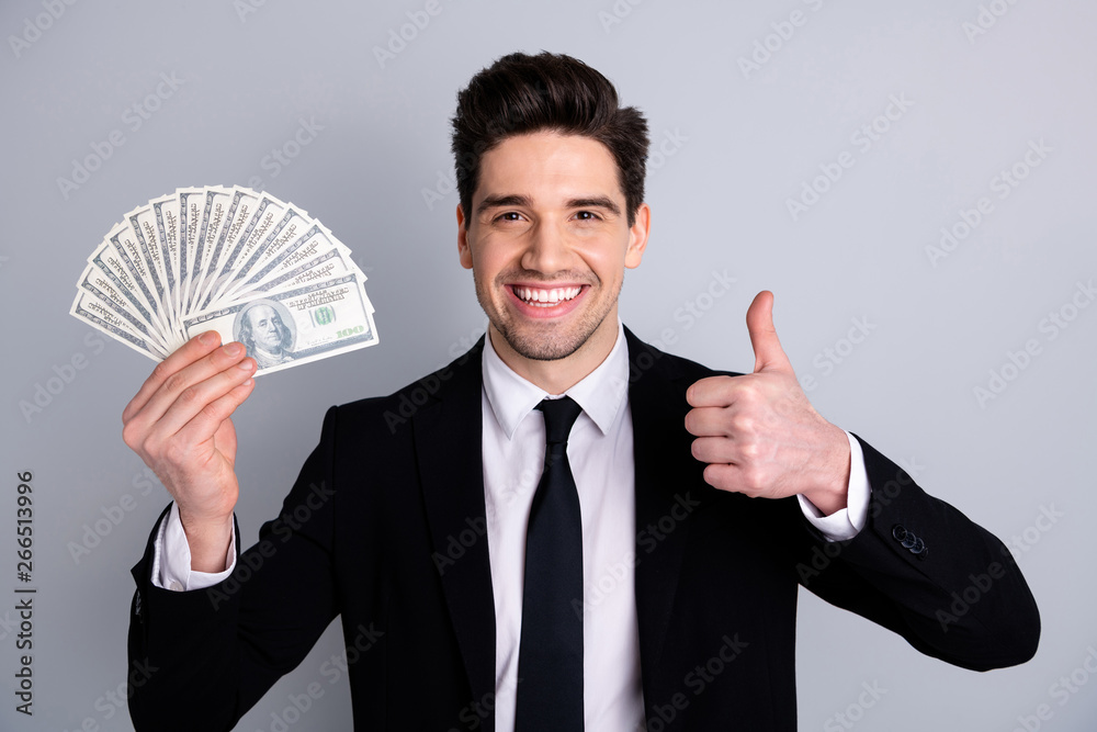 Close-up portrait of nice attractive cheerful guy sales manager financier banker economist holding in hand currency lottery credit loan showing thumbup isolated over light gray background Close-up portrait of nice attractive cheerful guy sales manager financier banker economist holding in hand currency lottery credit loan showing thumbup isolated over light gray background