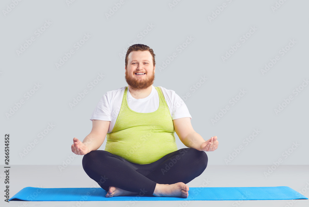 Positive fat man Yogi does yoga exercises a gray background. Stock